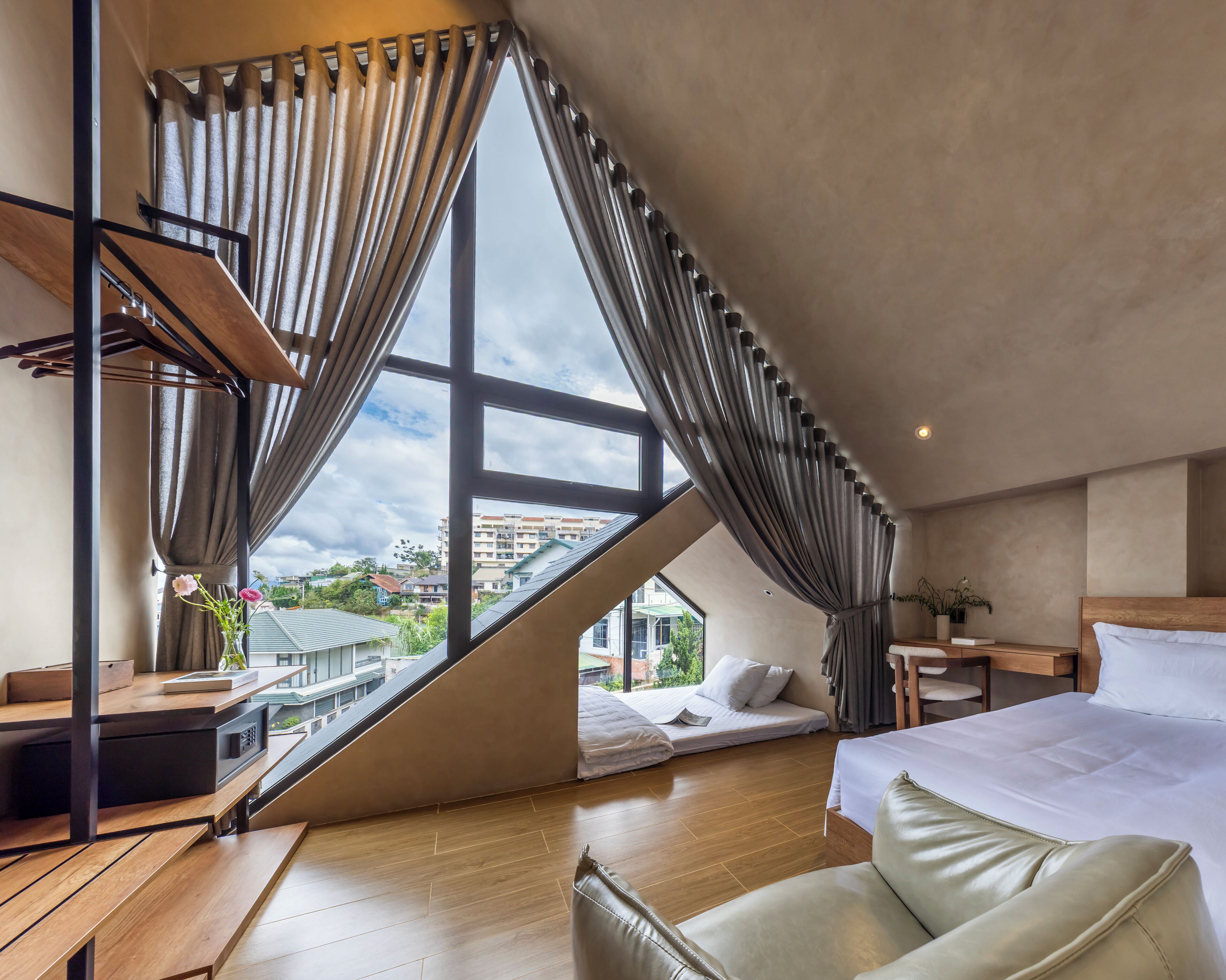Een moderne slaapkamer met een schuine kap, een groot raam met gordijnen, een bed, een bank en een kleine tafel.
