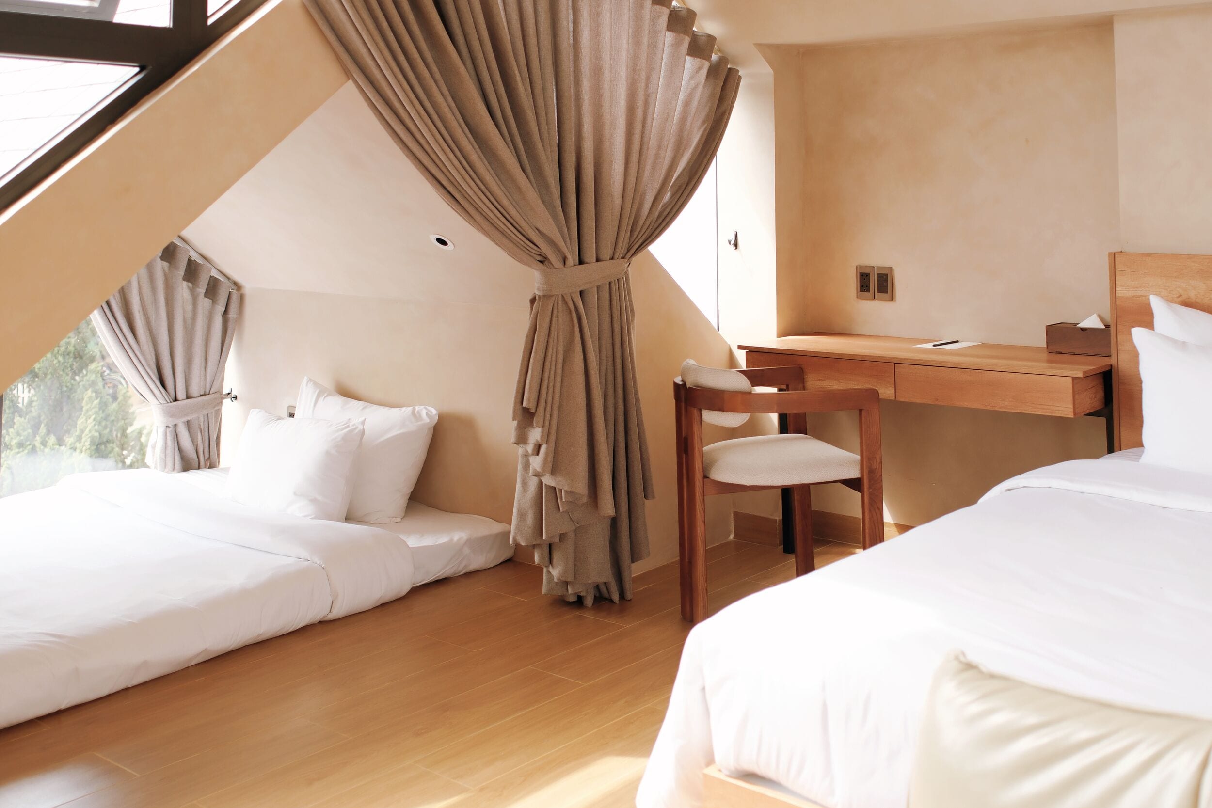 A bedroom with a sloped ceiling, a wooden desk, a chair, and two beds.