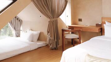 A bedroom with a sloped ceiling, a wooden desk, a chair, and two beds.