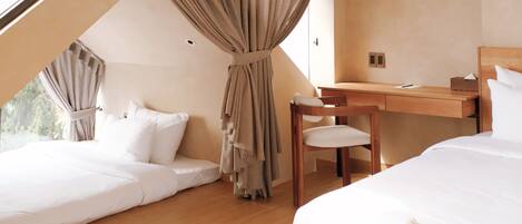A bedroom with a sloped ceiling, a wooden desk, a chair, and two beds.