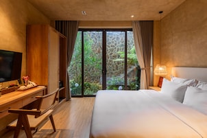 Una camera d'albergo con un letto, una scrivania, una televisione e vista sul verde attraverso una porta in vetro.