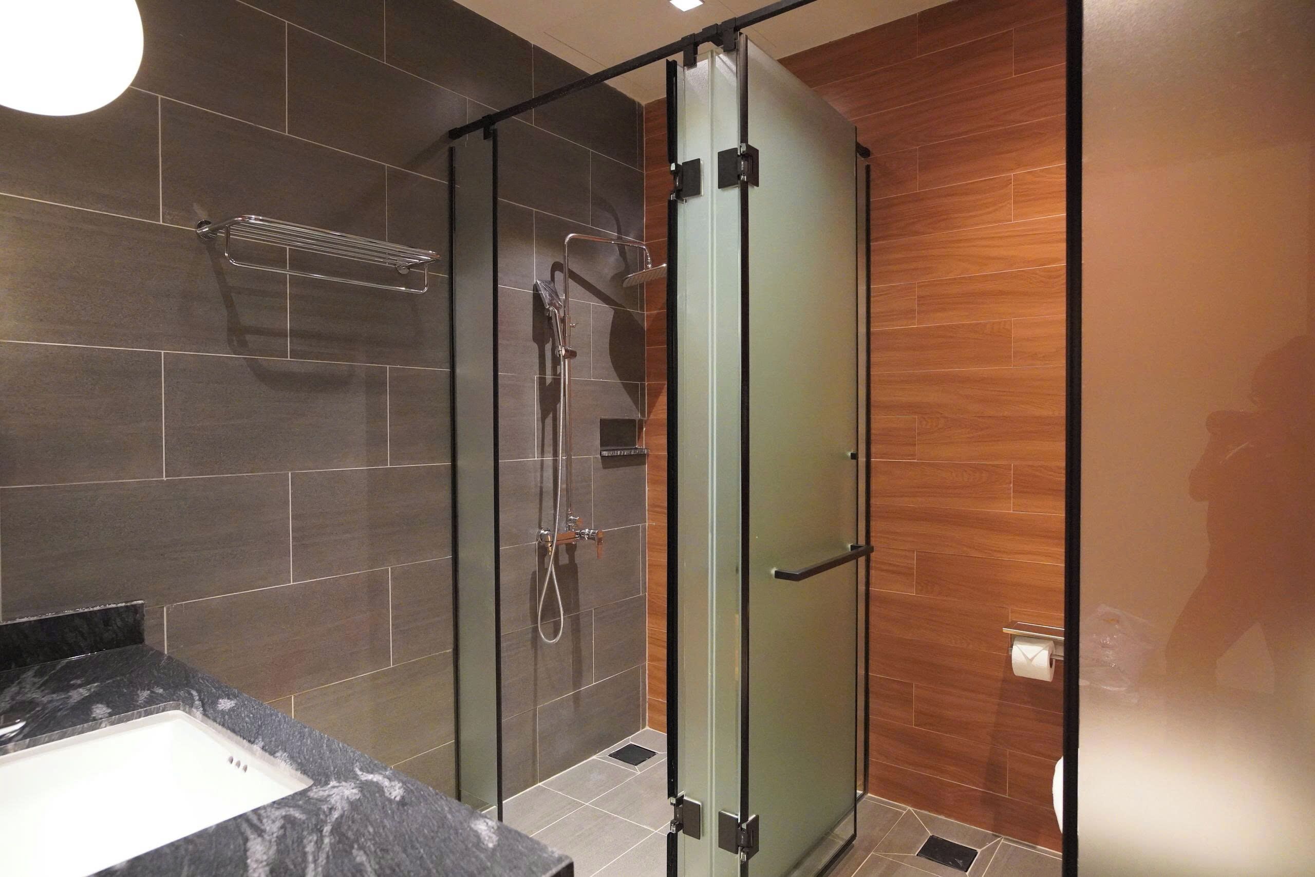 A modern bathroom with a glass-enclosed shower, a marble sink, and wooden flooring.