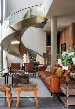 Un salon moderne avec un escalier à volutes, un canapé en cuir, une table basse en bois et un vase rempli de fleurs.