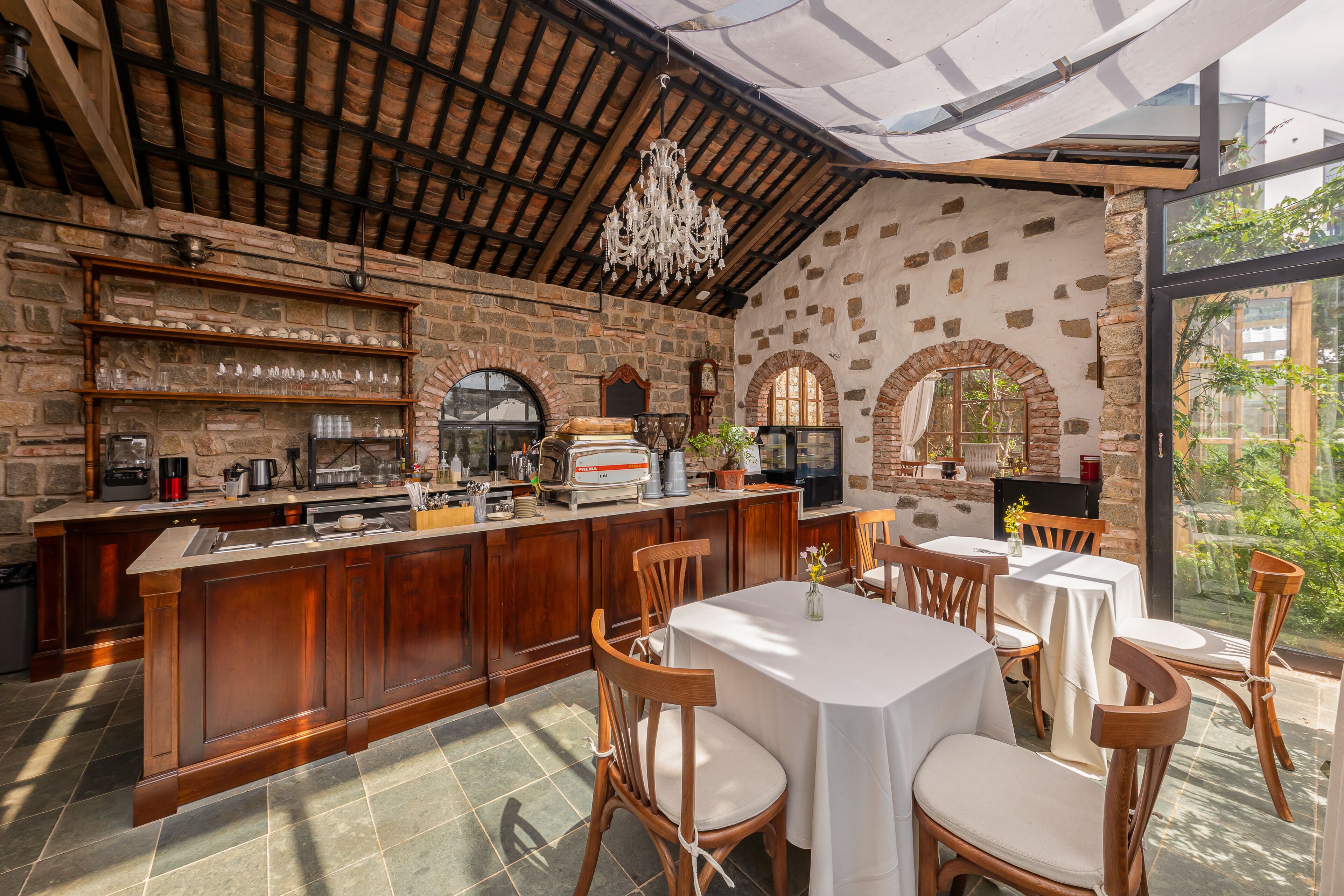 A rustic kitchen with a wooden bar, stone walls, and a chandelier.