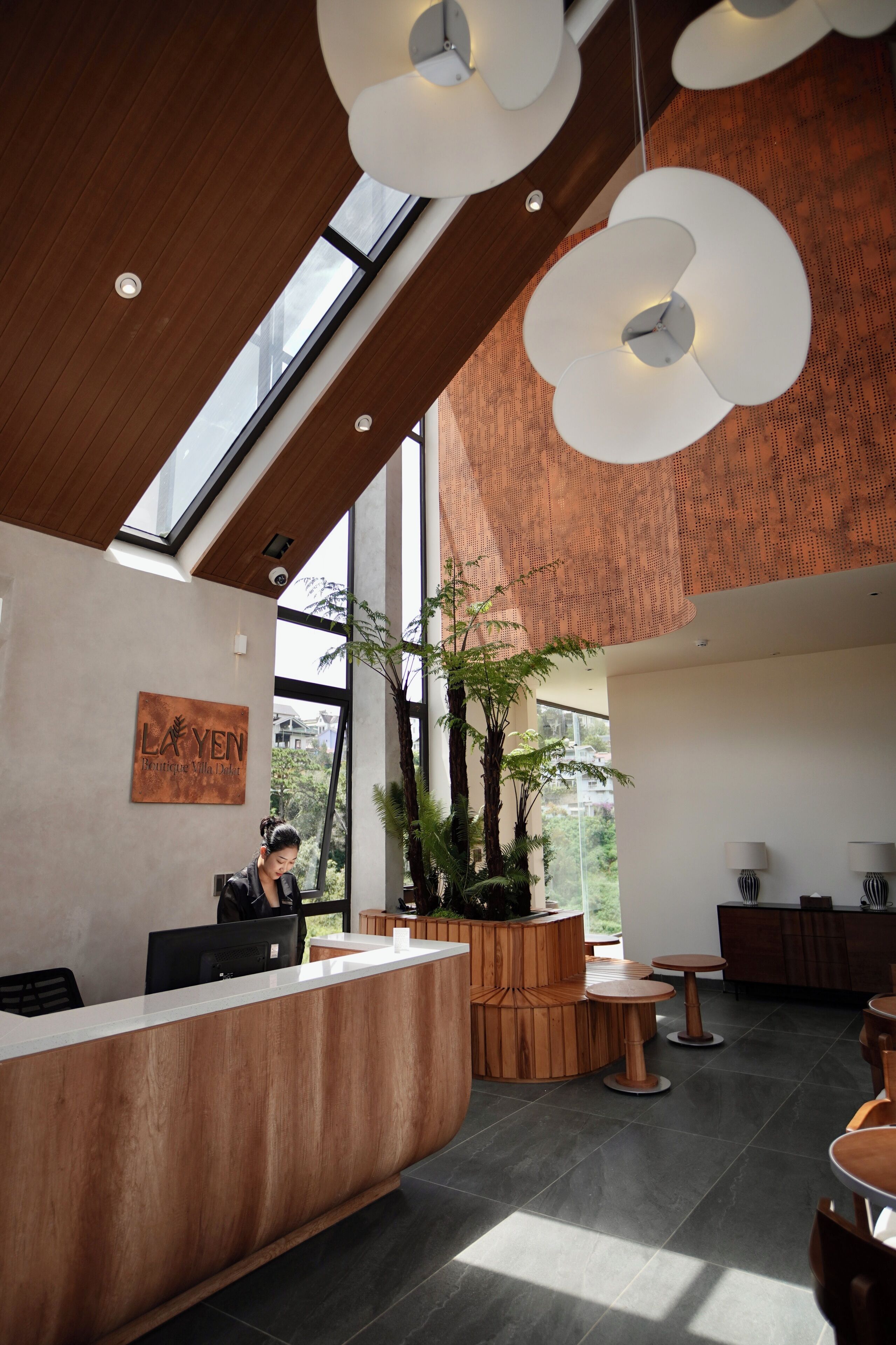 A modern reception area with a wooden reception desk, a large potted plant, and a seating area with round tables.
