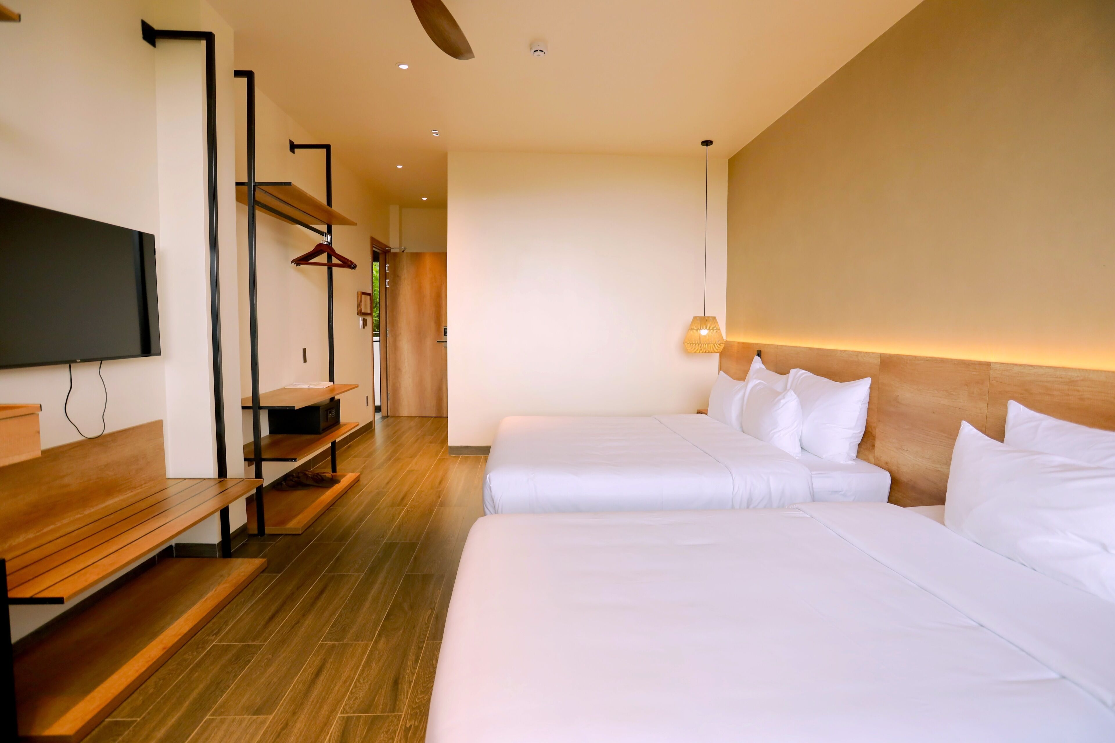 Een hotelkamer met twee bedden, een televisie, een houten bankje en een kapstok.