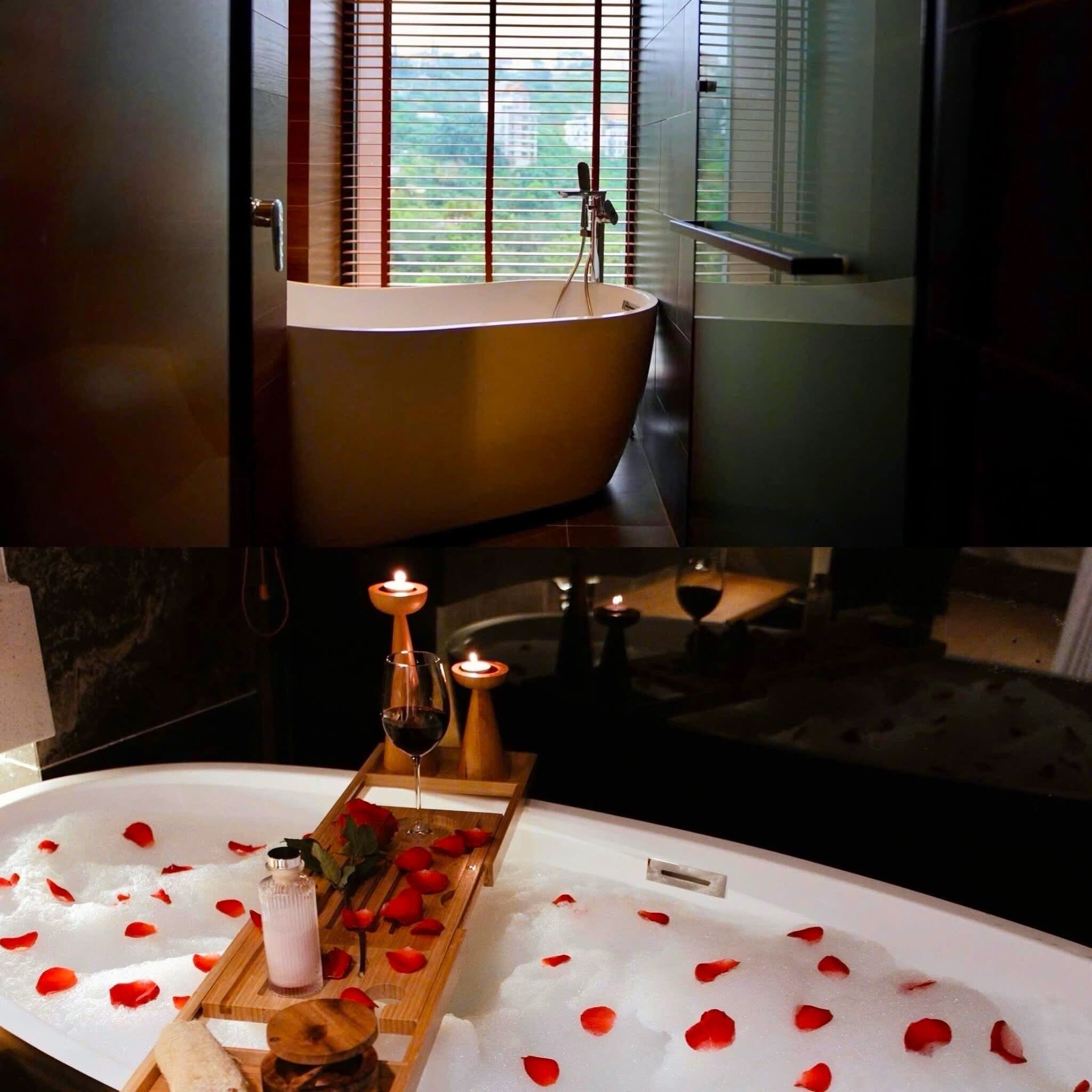 Una bañera con pétalos de rosa y velas, una bandeja con una copa de vino, y una ventana con persianas.