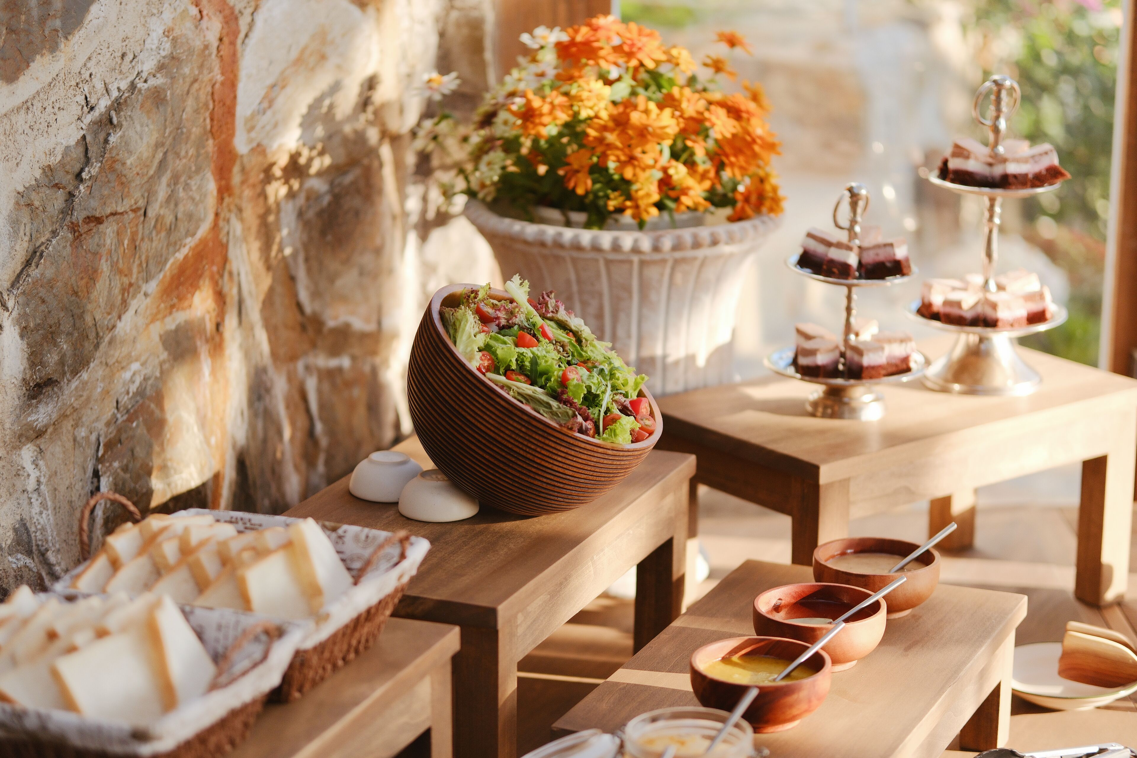 A wooden table with a salad bowl, dessert trays, and small bowls with spoons.