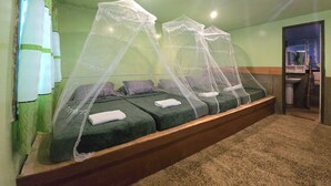 Une chambre avec deux lits protégés par des moustiquaires, un lavabo et un miroir dans un coin.
