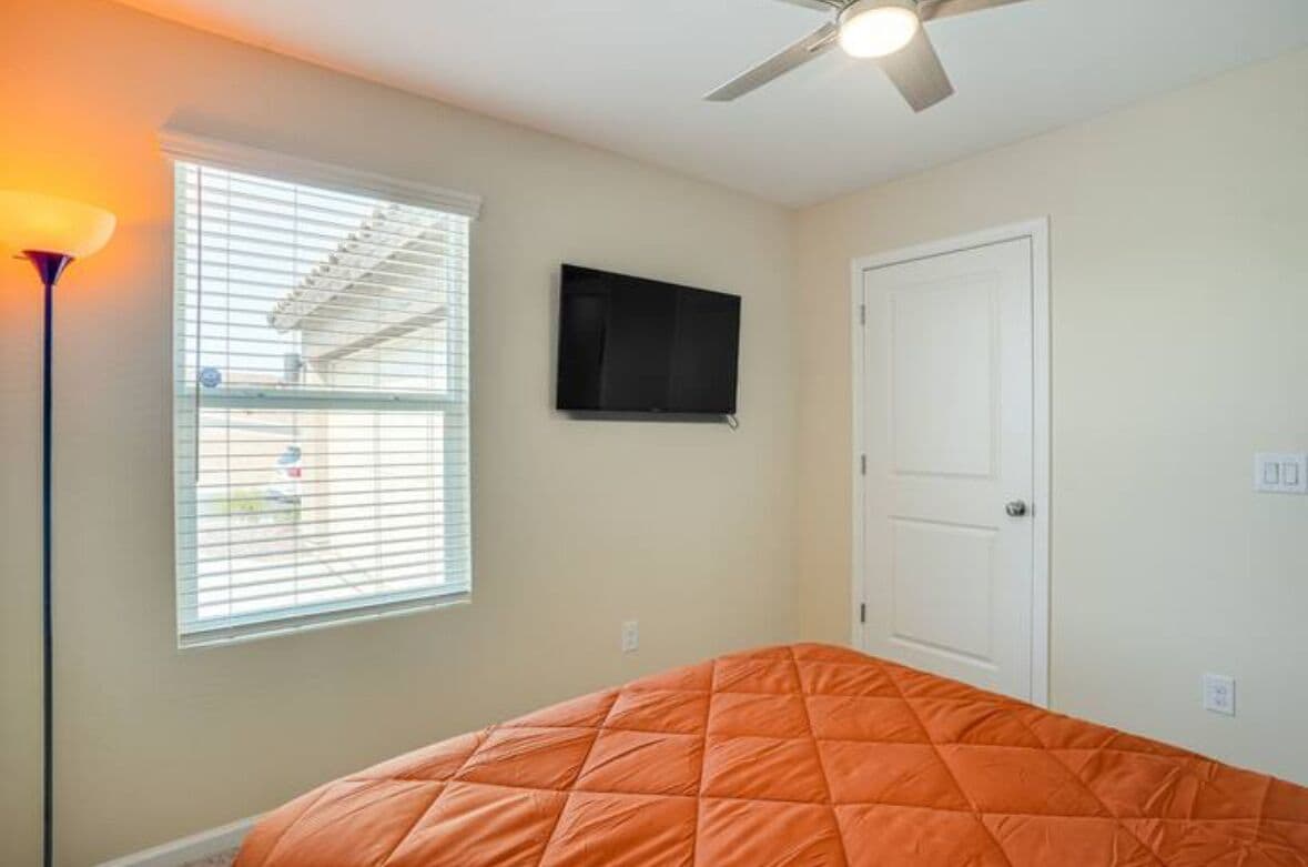Une chambre à coucher avec un lit, un ventilateur de plafond, une télévision et une fenêtre avec des stores.
