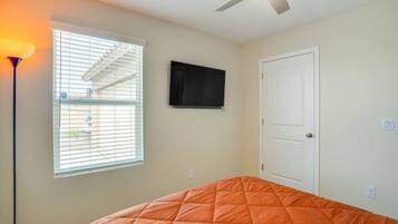 Une chambre à coucher avec un lit, un ventilateur de plafond, une télévision et une fenêtre avec des stores.