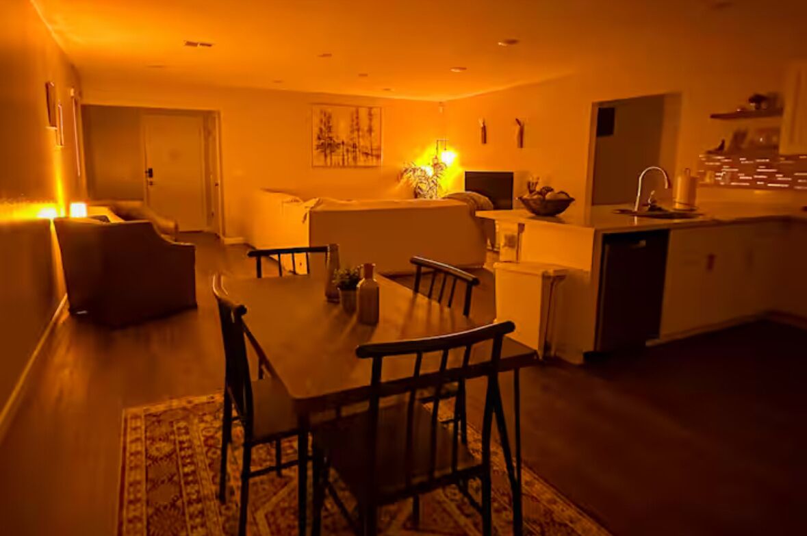 A cozy living room with a dining table, chairs, and a sofa. There is a kitchen area with a sink and cabinets.