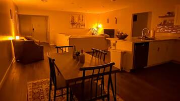 A cozy living room with a dining table, chairs, and a sofa. There is a kitchen area with a sink and cabinets.