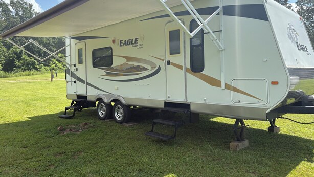 A white RV with "Eagle Super Lite" branding, a covered living area, and a side-mounted awning. - Branson Glamping - all set up for you (Branson)