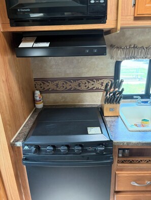 A compact kitchen with a black stove, a built-in oven, a microwave, and a small sink.