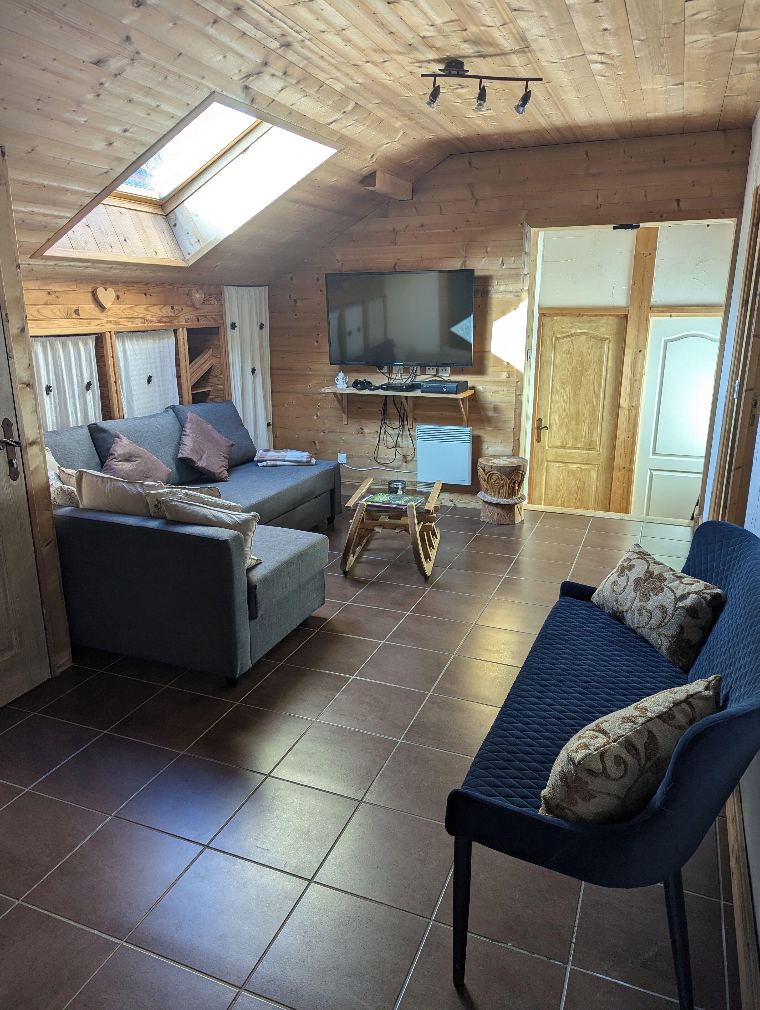 A cozy room with a sofa, a blue armchair, a TV, and a wooden ceiling.