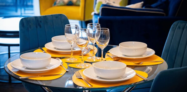 Una mesa de comedor dispuesta con cuencos blancos, copas de vino y posavasos amarillos.