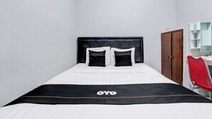 A single bed with a black and white bedspread, a wooden wardrobe, and a red chair. - OYO 3220 Samudra Guesthouse (Depok)
