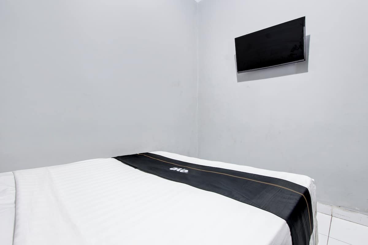 Una cama individual con colcha blanco y negro, un televisor de pantalla plana en la pared, y una pared blanca lisa.