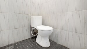 A small, white toilet in a corner with a tiled floor and walls. - OYO 3220 Samudra Guesthouse (Depok)