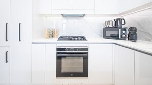 A modern kitchen with white cabinets, a built-in oven, a gas stove, a microwave, and a coffee maker. - Dubai Luxury Apartment w/ Pool & Gym, Near Cafes (Dubai)