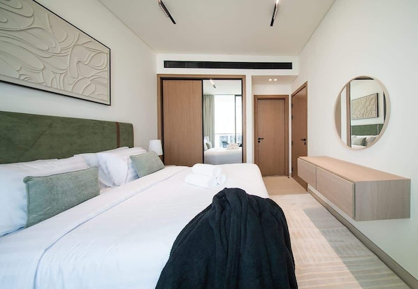 Ein modernes Hotelzimmer mit einem großen Bett, einem Nachttisch, einem Kleiderschrank und einem Spiegel an der Wand.