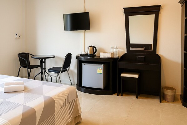 A hotel room with a bed, a desk, a chair, a small refrigerator, a mirror, and a trash bin.