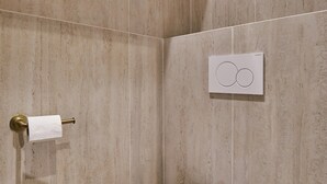 Une salle de bain moderne avec des toilettes blanches, un distributeur de serviettes et un panneau de commande fixé au mur.