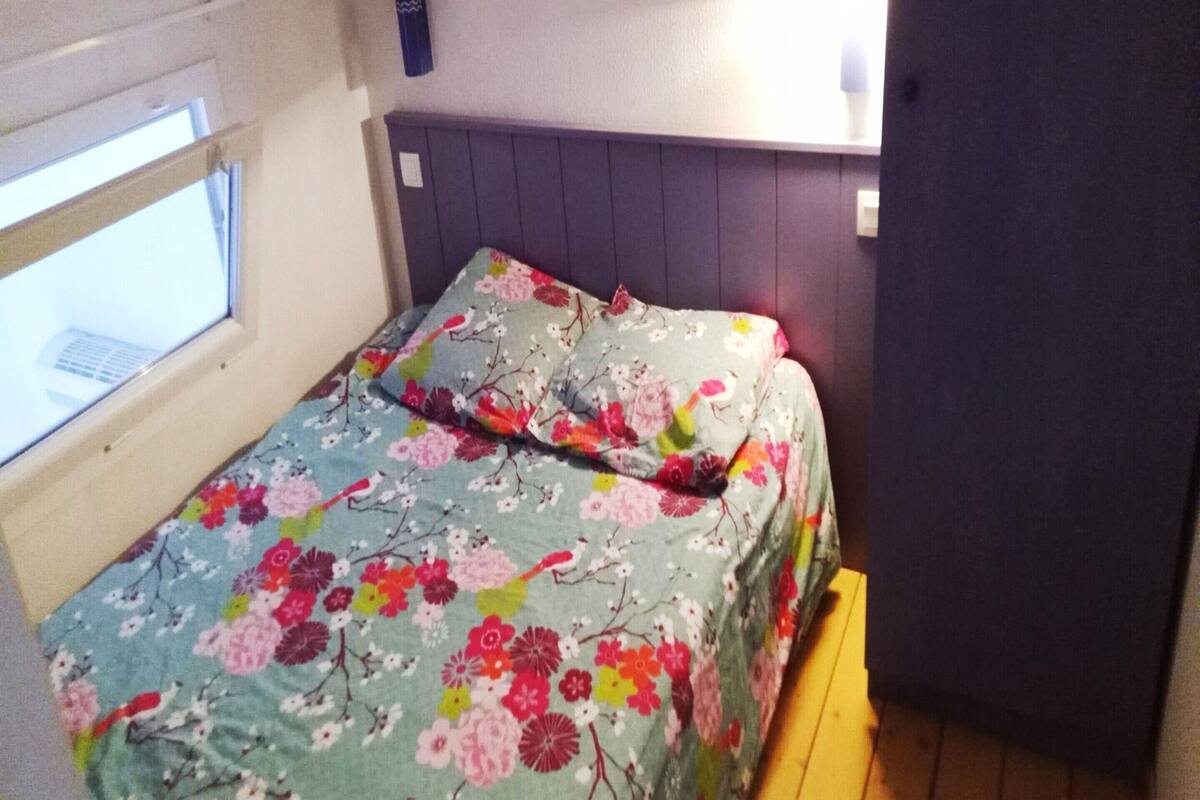 Une petite pièce, de taille modeste, comprenant un lit simple, une fenêtre et une lampe fixée au mur.