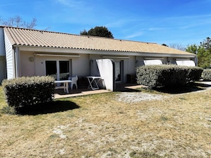 A single-story building with a tiled roof, a patio area with a table and chairs, and two well-maintained bushes. - Apartment on Ile D'oleron Near the Beach (Saint-Georges-d'Oleron)