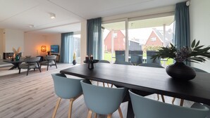 Een moderne eethoek met een donker houten tafel en lichtblauwe stoelen, een bloevas en uitzicht op een rood huis door grote ramen.