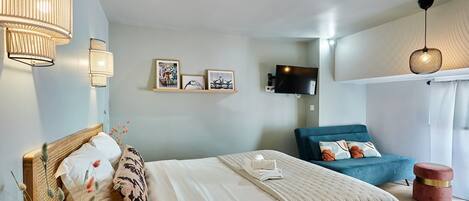 A bedroom with a bed, a TV, a blue sofa, and a red ottoman.