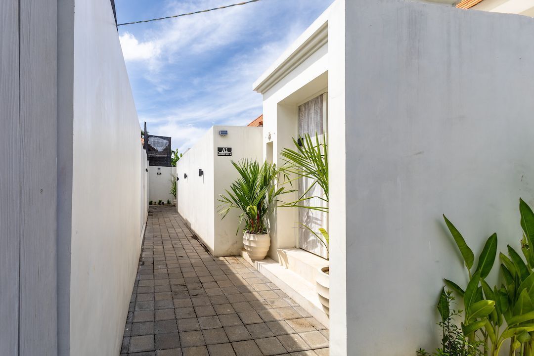 A narrow alleyway with white walls, a tiled floor, and potted plants.