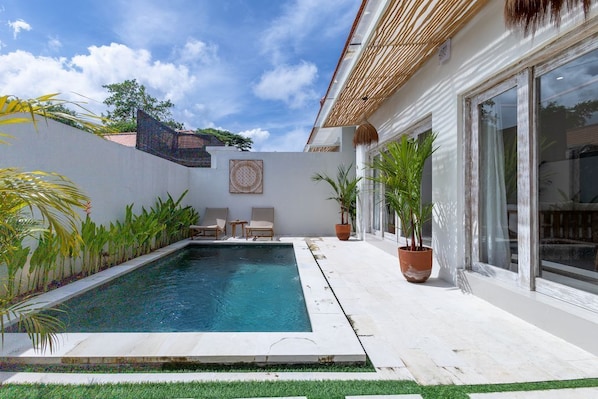 Una piscina con un muro blanco y una puerta de cristal a la derecha.