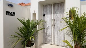A white building with a sign reading 'A1 ALINKO VILLA,' a door with a textured surface, and potted plants in the foreground. - Alinko Villa - 2BR Villa in Seminyak (Seminyak)