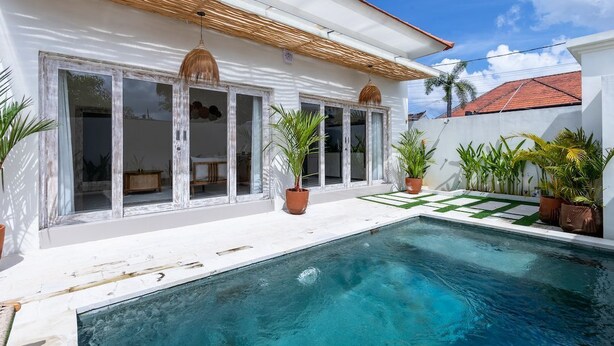 A poolside area with a clear blue pool, white walls, and potted plants. - Alinko Villa - 2BR Villa in Seminyak (Seminyak)