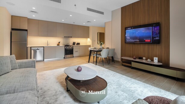 A modern living room with a sofa, coffee table, and a TV mounted on the wall. - Manzil - Cozy 1BR Waterfront Apartment  (Dubai)