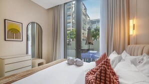 A hotel room with a bed, a desk, a chair, a large window, and a view of the outside. - Manzil - Cozy 1BR Waterfront Apartment  (Dubai)