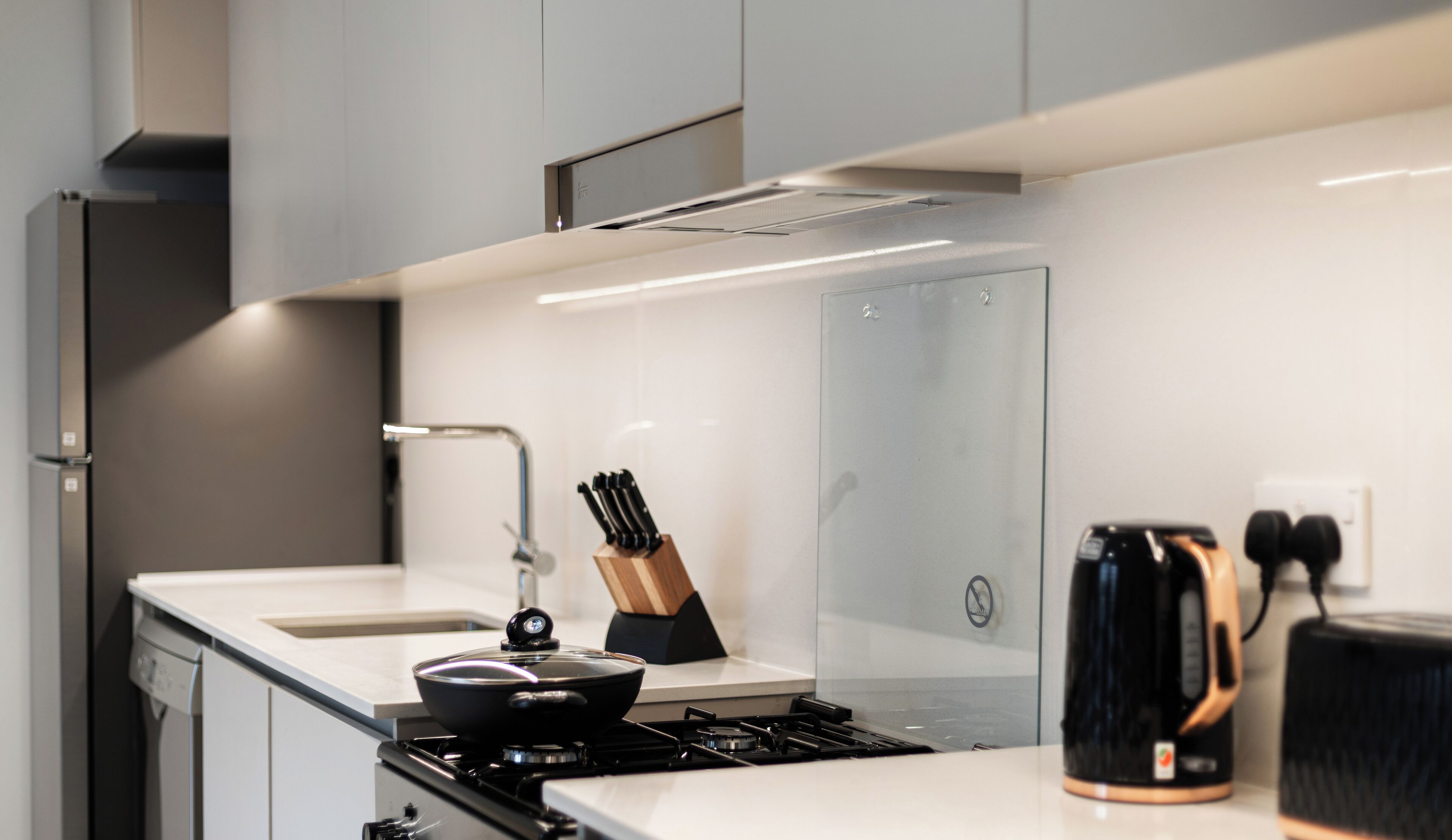 A modern kitchen with white cabinetry, a stainless steel range hood, a gas stove, a sink, and a knife block.