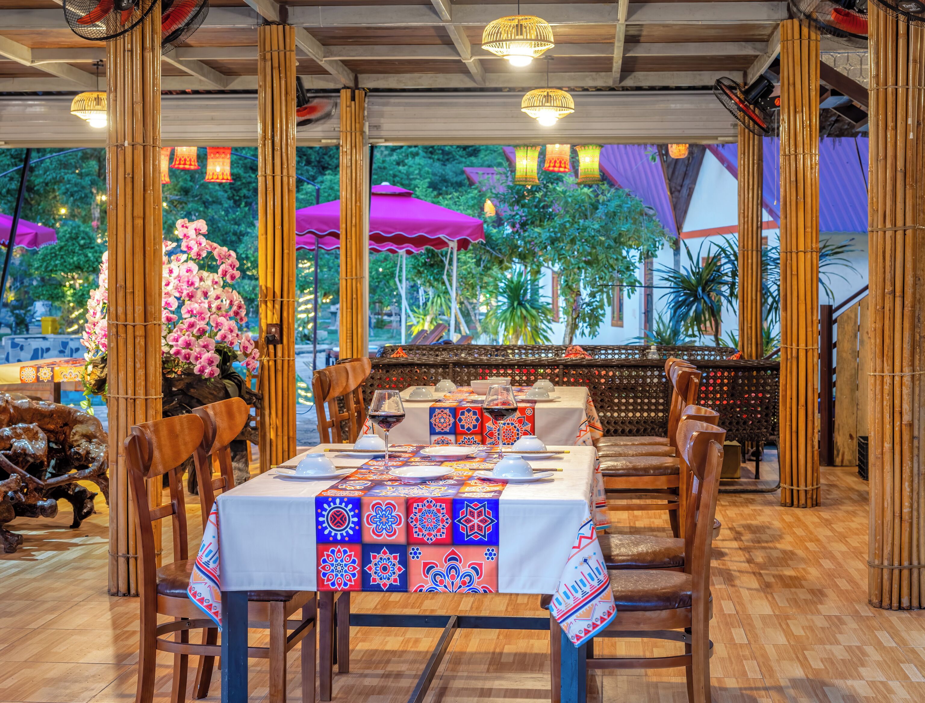 An outdoor restaurant with bamboo pillars, wooden tables, and chairs.