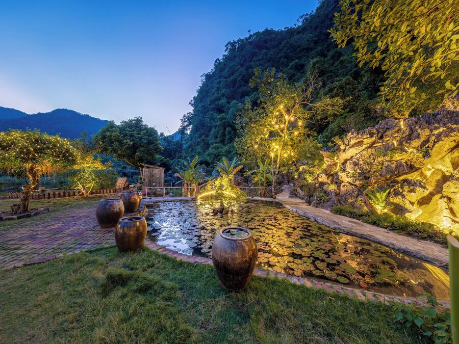 Um jardim tranquilo com lago, caminho de pedra e vasos grandes.
