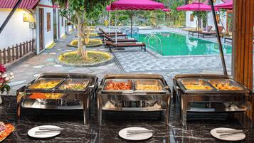 A buffet area with multiple food stations, a pool, and lounge chairs.