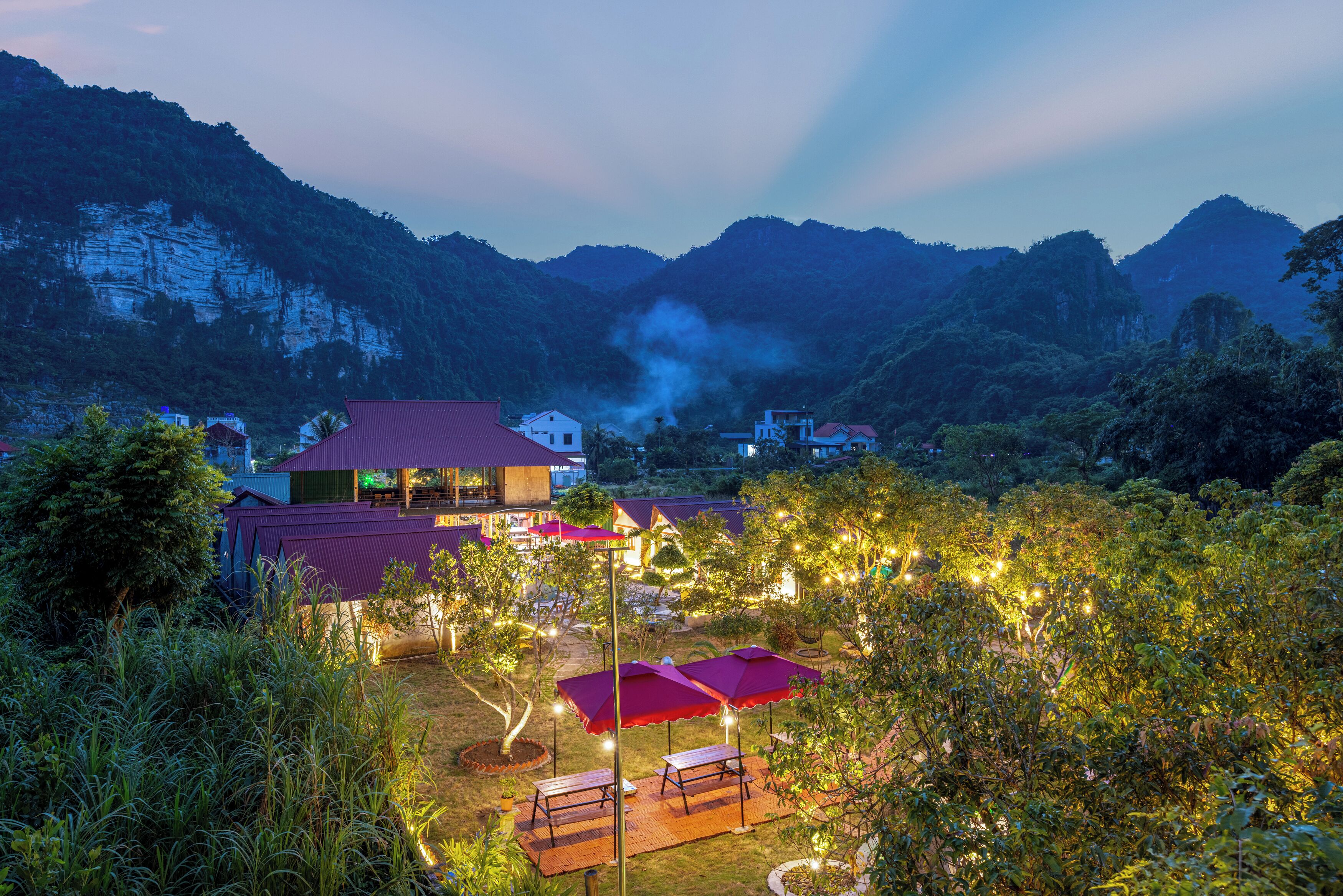 A resort with outdoor seating, a red-roofed building, and a mountainous backdrop.