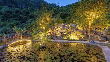 A serene pond with lily pads surrounded by a wooden bridge and illuminated trees.