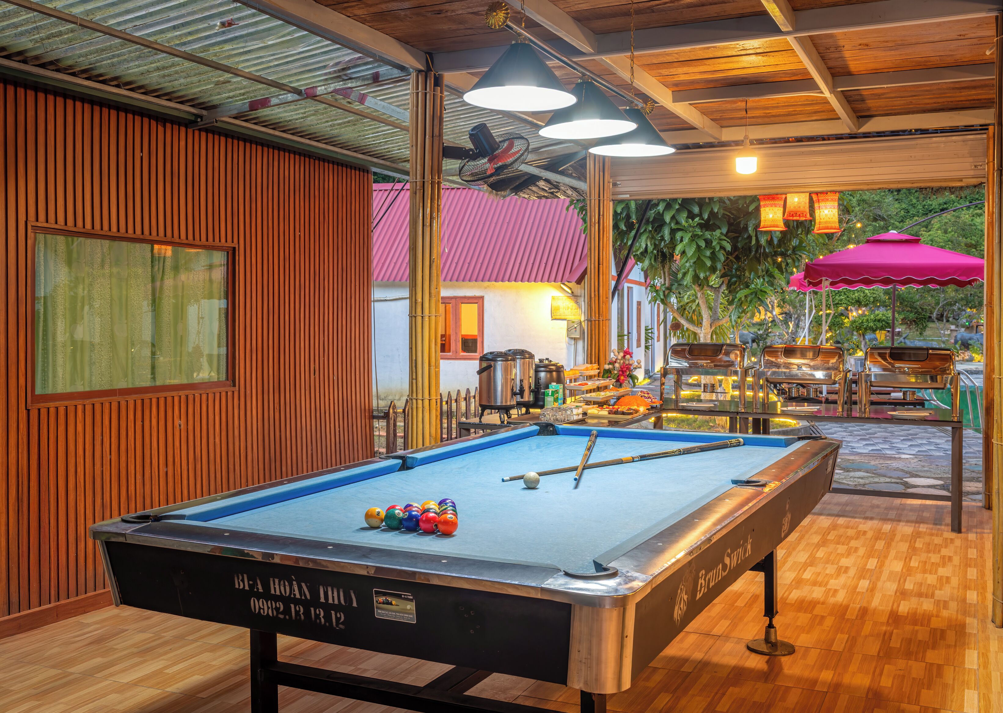 A pool table with billiard balls, a table tennis table, and a bar area with stools and a grill.