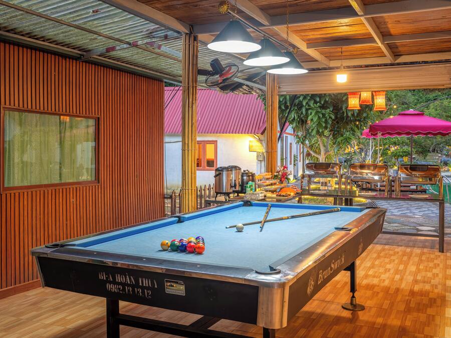 A pool table with billiard balls, a table tennis table, and a bar area with stools and a grill.