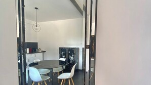 Un comedor moderno con una mesa redonda y cuatro sillas, un espejo grande en la pared y una zona de cocina al fondo.