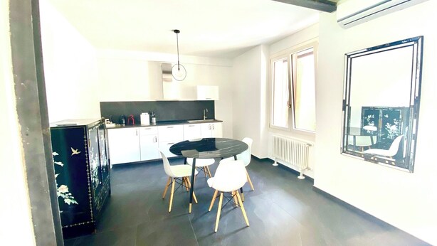 Una cocina moderna con armarios blancos, encimera negra y una mesa redonda con sillas blancas.