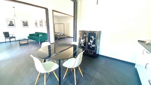 Un comedor moderno con una mesa redonda y dos sillas blancas, un sofá verde y un mueble negro con diseños florales.