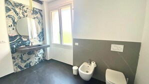 Un baño moderno con salpicadero de mármol, un lavabo pedestal, un bidé y un inodoro.